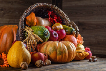 Thanksgiving day close up still life. Pumpkin harvest in wicker basket. Squash, vegetable autumn fruit, apples, and nuts on a wooden table. Halloween decoration fall design