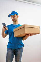 Delivery man with a box, smartphone. Courier in uniform cap and t-shirt service fast delivering orders. Young guy holding a cardboard package.