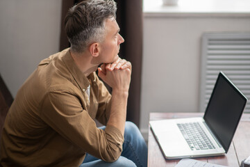 Man pensively looking at window sitting at laptop