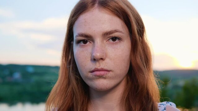 Confident Dreamer Face Beautiful Red Haired Young Girl Posing on Background of the Lake Nature at Sunset. Natural Child Beauty. Female has Long Ginger Hair, Freckled. Brown Eyes. Outdoor.