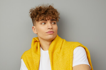 a funny young man stands on a light background in stylish clothes and looks thoughtfully to the side with his back against the wall