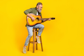 Full body portrait of positive peaceful aged man sitting chair hold play guitar isolated on yellow color background - obrazy, fototapety, plakaty