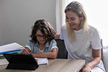 Mother and small son eyeglasses study online on tablet at home together lesson, prepare homework