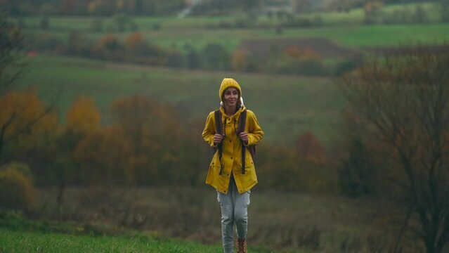 slow motion inspired young pretty woman hiker in yellow raincoat with backpack and beanie walking along firest in fields on hills enjoying nature beauty, freshness and freedom wonderful autumn woods.