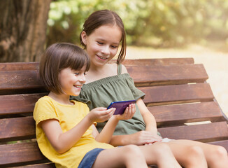 Deux filles heureuses regardant leur téléphone. Jolis enfants surfant sur Internet au parc