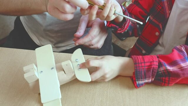 Happy father's day and childhood concept. Close-up of the hands of a man father and child work with hand tools, using a screwdriver, assembling a wooden constructor at home at the table