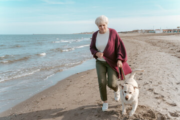 Gray-haired female walking with her dog on the seashore