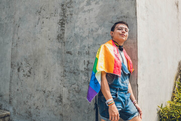 gay teen man with lgbt flag on gray city wall in sunny day
