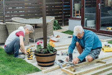 Adult son and father carpenter working together, handle wooden timbers in the garden. Patio...