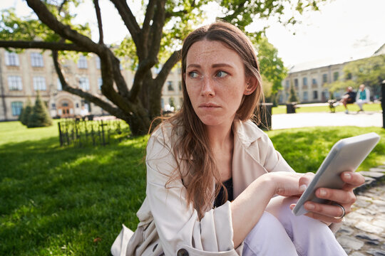 Lady with phone in hands sits in park on pavement