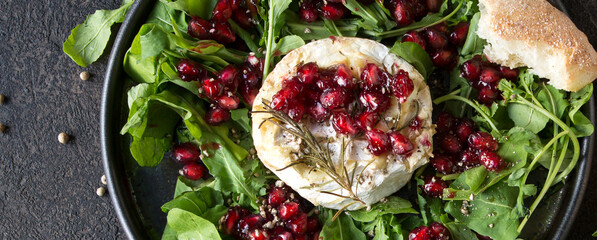 a plate of baked brie cheese with lingonberry sauce and pomegranate on a dark table