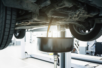 Engine oil change in car service. Auto is on hydraulic lift in garage workshop, process of draining...