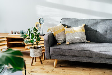Stylish living room interior with designer console with decor and gray sofa with graphic pillows. White walls, green plants in the pots. Light wooden oak parquet. Modern Scandinavian style interior. © okrasiuk