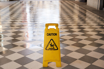 Wet exterior floor with black and white rhombuses with a yellow plastic sign with a warning symbol...