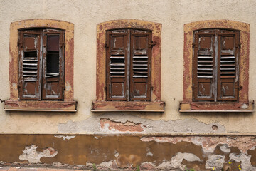 View of an old house facade in need of renovation with three windows closed with shutters