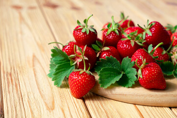 Delicious juicy strawberries on wooden board on wooden background. Farm strawberry harvest. Healthy eating, raw diet and detox food concept. Natural source of vitamins and antioxidants. Copy space.