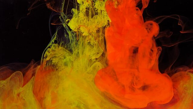 Stream of red and yellow paint dissolves in a transparent space on a black background.