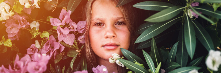 portrait face of candid beautiful little kid girl of eight years old on background of green plants and pink flowers during a summer vacation travel. gen z mental health concept. banner. flare