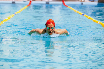 Live portrait of young woman, swimmer in swimming cap and goggles practicing at public swimming-pool, outdoors. Sport, power, energy, style, hobby concept.