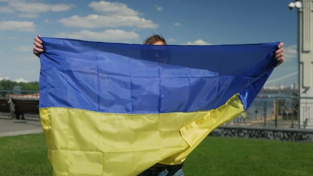 White man in sunglasses lifting Ukrainian national flag in front of him and backing up his country. Handsome male model showing large blue and yellow flag and holding it in slow motion on a sunny day
