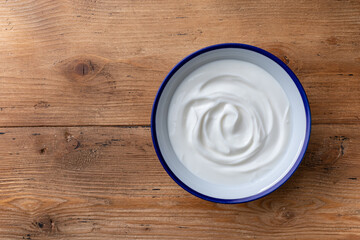 Greek yogurt in bowl on wooden rustic table top view.