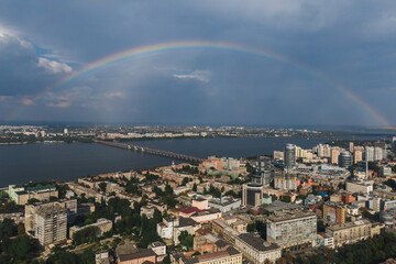 Beautiful rainbow after the rain on the blue sky and clouds over the city. An amazing natural phenomenon when sunlight is combined with rain. Photo taken from a drone