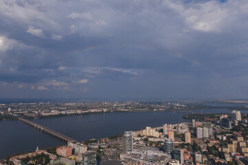 Beautiful rainbow after the rain on the blue sky and clouds over the city. An amazing natural phenomenon when sunlight is combined with rain. Photo taken from a drone