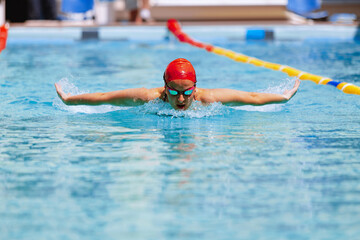 Live portrait of young woman, swimmer in swimming cap and goggles practicing at public swimming-pool, outdoors. Sport, power, energy, style, hobby concept.