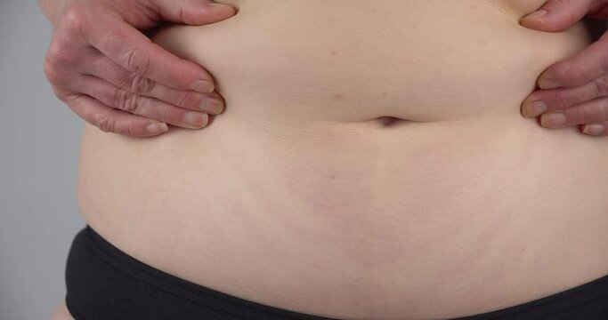 Slow motion of woman in innerwear pressing bare abdomen with hands and showing unwanted belly fat. Close up.