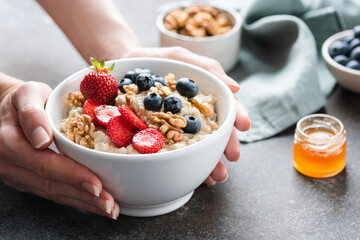 Oatmeal porridge with strawberry blueberry and walnuts in female hands, closeup view. Healthy eating, dieting, weight loss concept