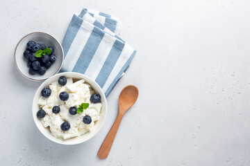 Cottage cheese with blueberries in bowl on grey concrete background, top view. Homemade soft white...