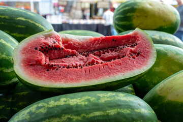 Fresh elongated watermelon with a transverse cut showing a pink chunky inside with lots of black...