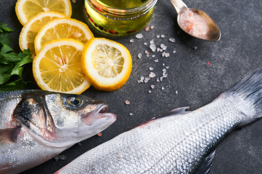 Sea Bass raw. Fresh sea fish bass with salt, pepper, parsley, olive oil and lemon on dark concrete rustic background. Fresh fish ready to cook. Food cooking background. Top view, copy space.