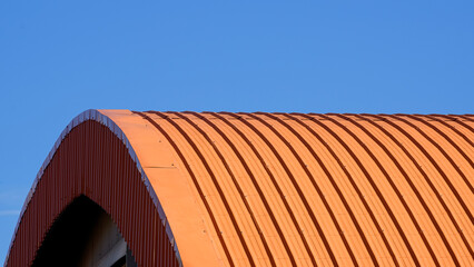 Orange curved corrugated steel roof against blue clear sky background