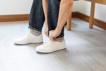 Man tie the shoelace of white sneakers sit on wood bench at home.