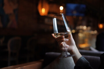 Female hand with french manicure holding a glass with wine on naturally blurred background. Woman in restaraunt. Luxury pasttime, celebration concept. 