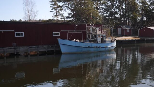 A stationary footage of an old fishing boat docked in a lake in Sweden and has been left untouched. Its reflection is clearly seen on the surface of the water and the weather is fine.