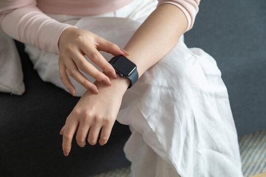 Close up of woman checking smart watch sitting on sofa at home.