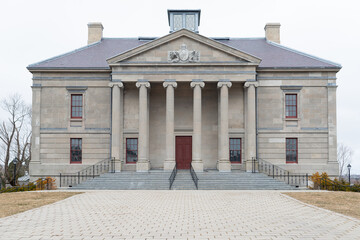 A wide brick entrance to a large courthouse, justice or government style building. There's a tall red door, grey marble steps, black handrails, tall windows, round pillars, and a beige exterior wall.