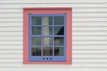 A single vintage storm window with 12 small panes, a purple wooden frame, and pink trim in a white...