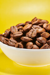 Roasted coffee beans in bowl isolated close up on yellow background, clipping path