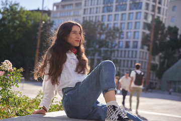 Fototapeta premium Portrait of a young woman sitting alone in the city in the background. Caucasian young adult with long hair
