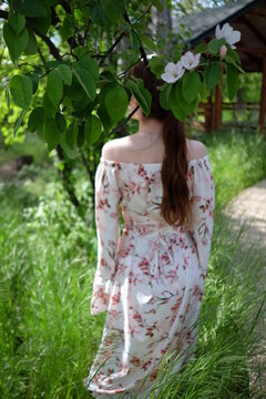 a girl in a dress with a floral print stands with her back under a flowering tree
