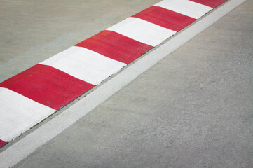 Footpath road. Red and white concrete sidewalk curb with green grass. View of Circuit. signs on a road. racetrack with white lines. White and red strip no Parking Sign on Footpath road.