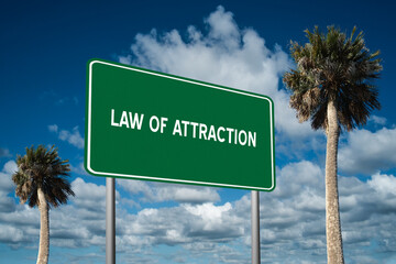Fototapeta premium Highway sign with the words Law of Attraction on a beautiful blue sky background with palm trees. Motivational concept for finding what we want on the journey of life.