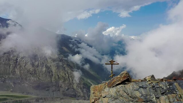Orbit aerial shot of Orthodox cross on Mount Kazbek slope (3500 m) above Mayly and Kolka glaciers on sunny summer day. North Ossetia–Alania, Russia.