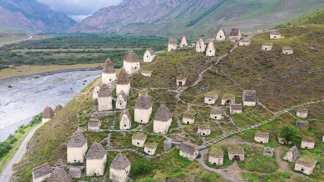 Aerial footage of medieval necropolis on the bank of Gizeldon river on cloudy summer day. Dargavs village, North Ossetia, Caucasus, Russia.