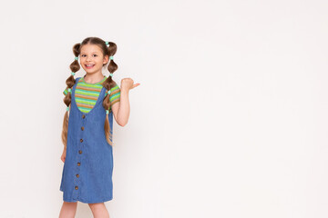 A little girl points her thumb at your ad on a white isolated background. A beautiful princess with long hair in a summer sundress.