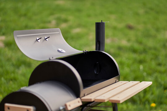 New smoker barbecue grill. Equipment for cooking and smoking. Meadow in Background.