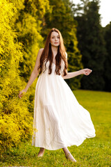 Fototapeta na wymiar Ginger woman in white dress dancing at a park
